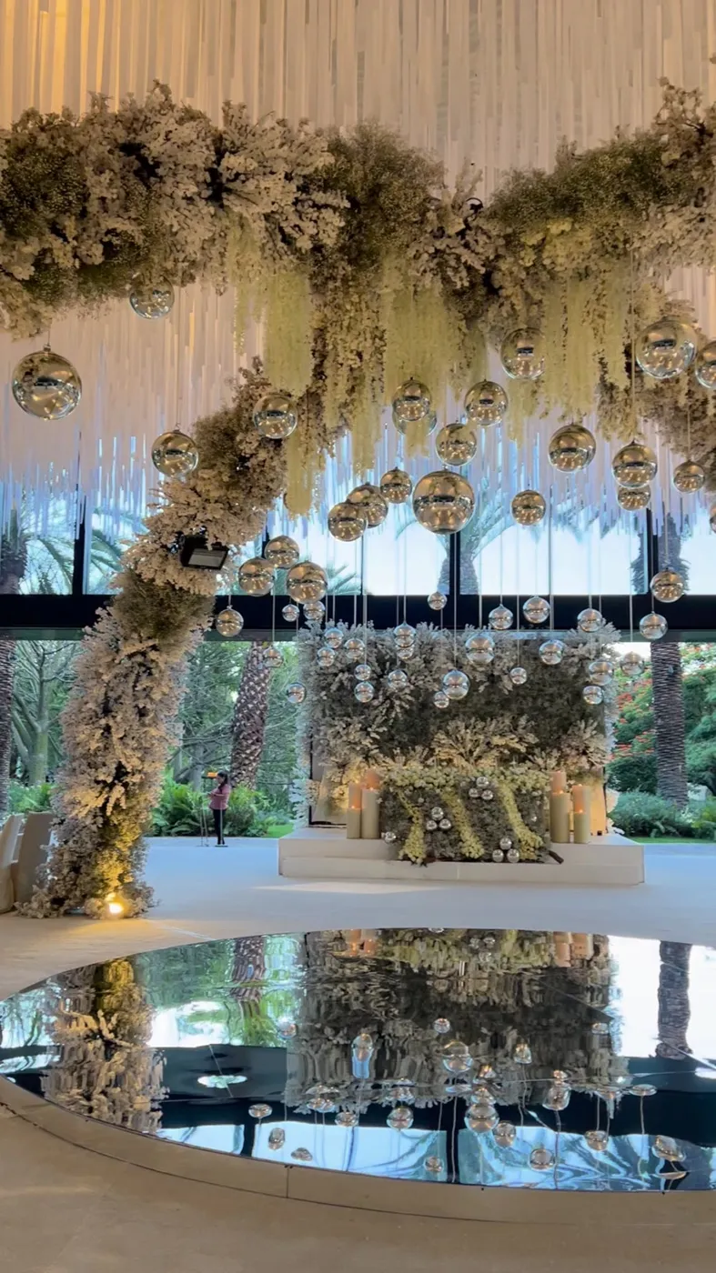 Pasillo bajo un arco floral doble con cielo de tiras de tela blanca y esferas de espejo